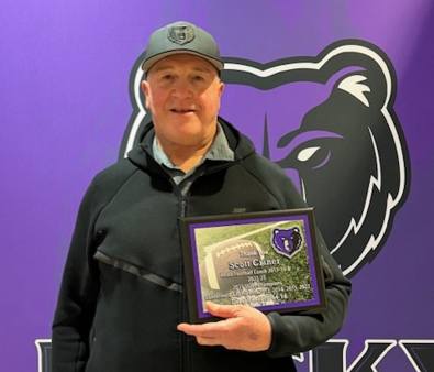 A photo of Coach Criner holding his football coach award up in front of a Rocky Mountain logo.