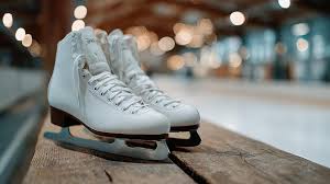 A pair of white figure skates rests on a weathered wooden bench at a local ice rink