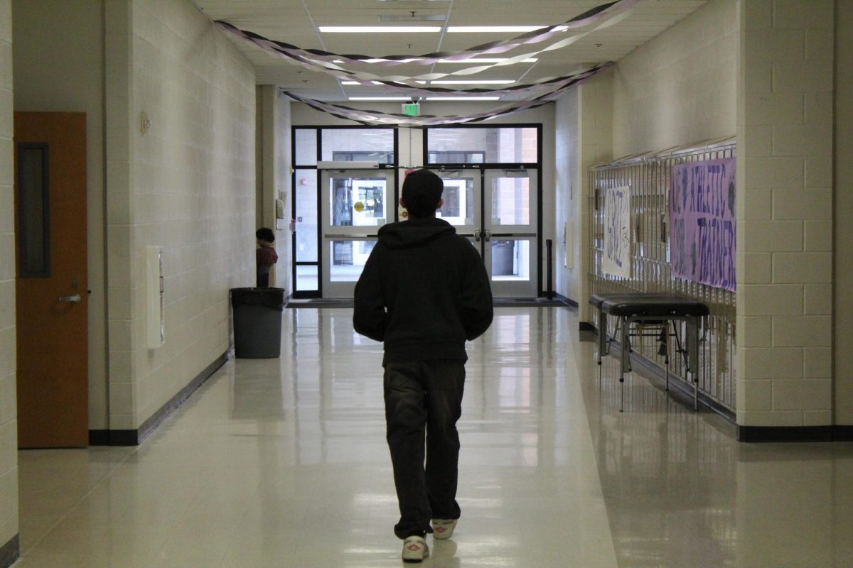 A student walking down a hallway towards a set of doors